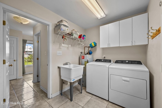 clothes washing area featuring cabinet space, water heater, washer and dryer, light tile patterned flooring, and baseboards