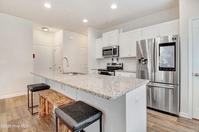 kitchen with a sink, stainless steel appliances, a kitchen breakfast bar, light wood finished floors, and white cabinetry