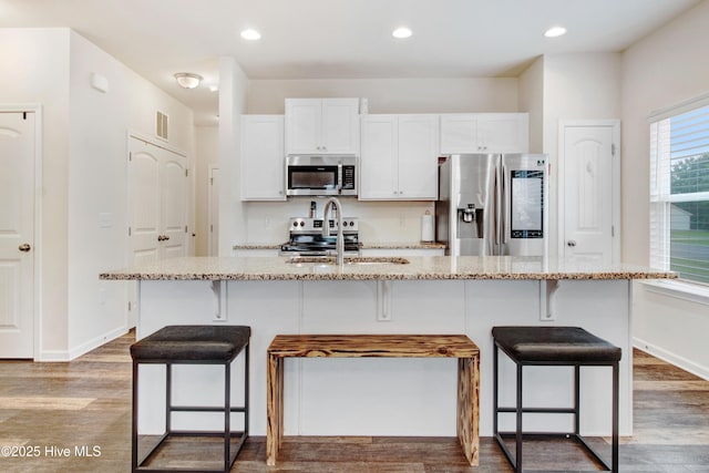 kitchen with a sink, stainless steel appliances, white cabinetry, and light stone countertops