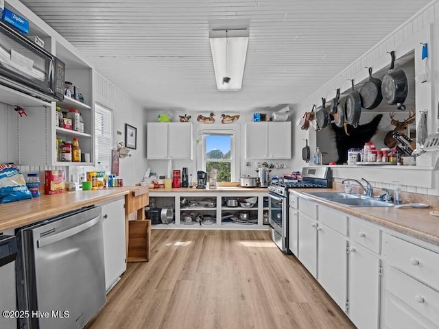 kitchen with appliances with stainless steel finishes, a sink, open shelves, white cabinets, and light wood-type flooring