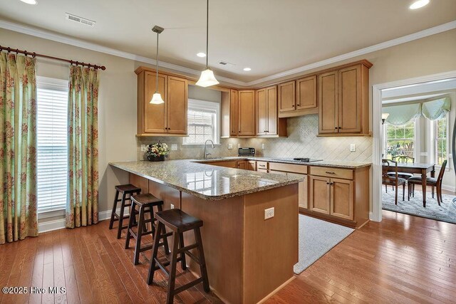 3284 Gardenwood Dr, Leland, NC 28451 - kitchen featuring a sink, a kitchen breakfast bar, hardwood / wood-style flooring, a peninsula, and light stone counters