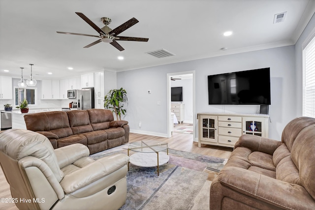 living area featuring a ceiling fan, recessed lighting, light wood-style flooring, baseboards, and crown molding