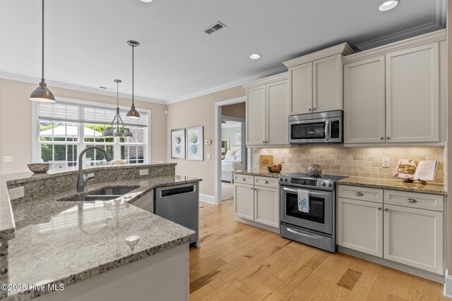 kitchen with appliances with stainless steel finishes, a sink, crown molding, tasteful backsplash, and light wood finished floors