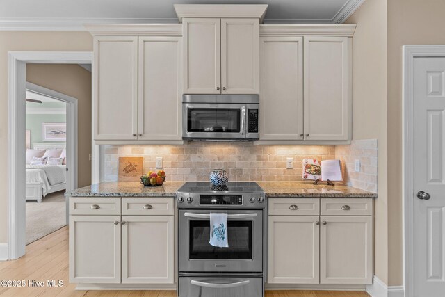 kitchen featuring appliances with stainless steel finishes, decorative backsplash, light stone counters, ornamental molding, and light wood-type flooring