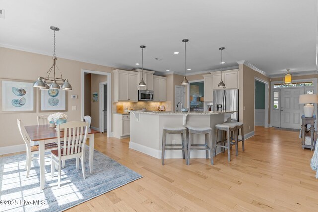 kitchen featuring appliances with stainless steel finishes, decorative backsplash, a kitchen island with sink, a breakfast bar, and ornamental molding