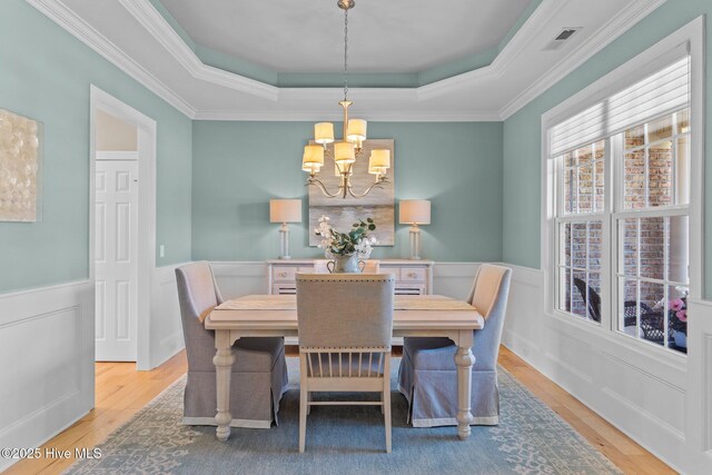 dining room with a chandelier, a tray ceiling, wood finished floors, wainscoting, and crown molding