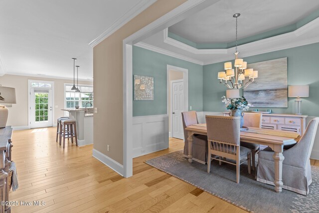 dining area with ornamental molding, a tray ceiling, light wood-style flooring, a chandelier, and wainscoting