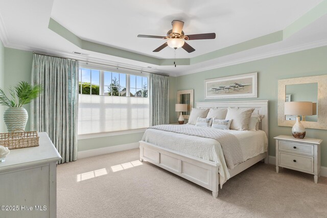 bedroom with a raised ceiling, light carpet, ornamental molding, baseboards, and ceiling fan