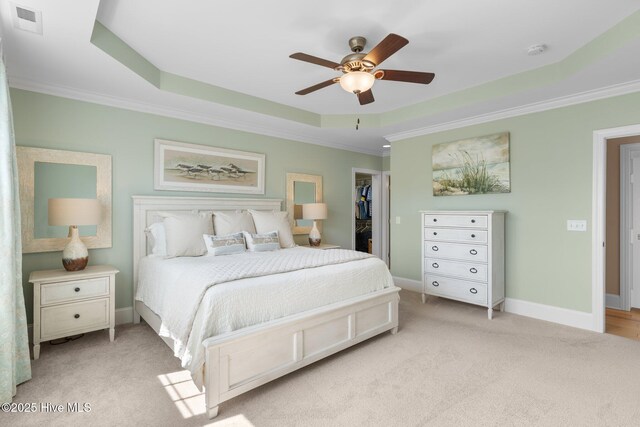 bedroom with ornamental molding, a raised ceiling, light carpet, a spacious closet, and baseboards