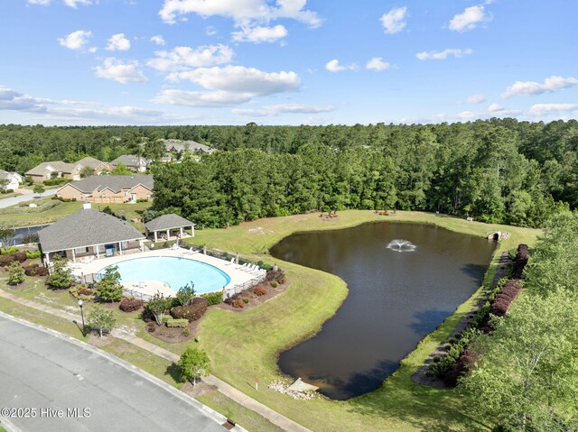 drone / aerial view of a heavily wooded area, a nearby body of water, and a pool area
