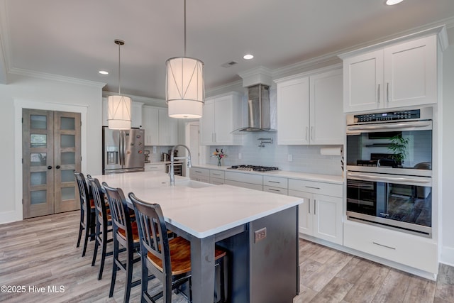 374 Yucca Ln, Wilmington, NC 28412 - kitchen featuring appliances with stainless steel finishes, wall chimney range hood, light countertops, white cabinetry, and tasteful backsplash