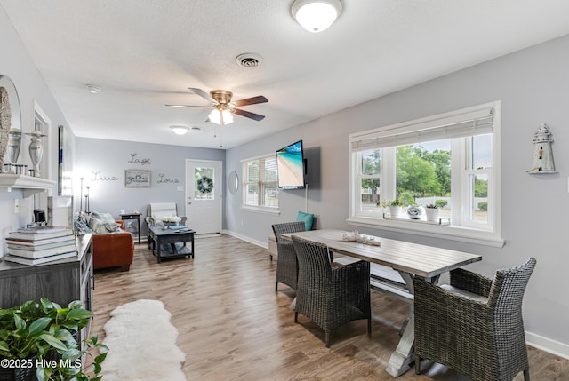 dining area with ceiling fan, light wood-type flooring, baseboards, and a textured ceiling