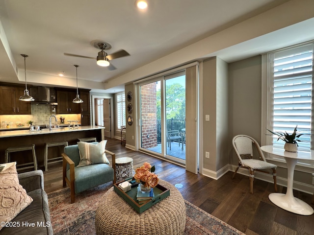 living area with a tray ceiling, baseboards, a ceiling fan, and dark wood-style floors