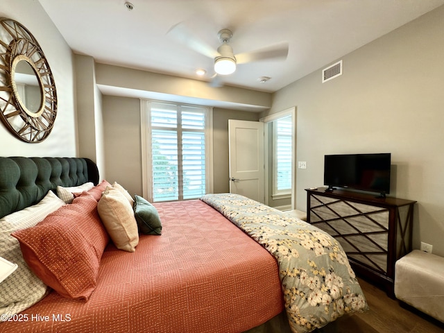 bedroom featuring a ceiling fan, multiple windows, visible vents, and wood finished floors