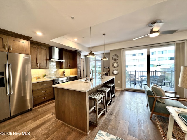 kitchen with a sink, stainless steel appliances, a kitchen breakfast bar, wall chimney exhaust hood, and light countertops