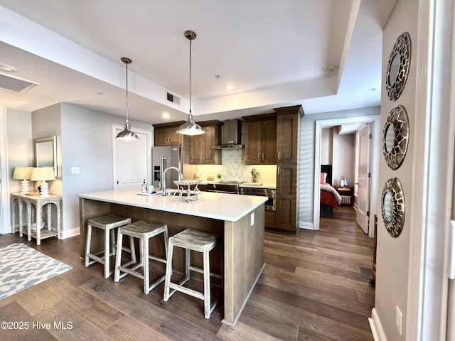 kitchen featuring wall chimney range hood, visible vents, an island with sink, light countertops, and high end refrigerator