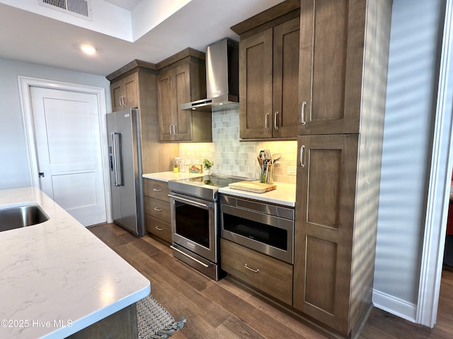 kitchen featuring stainless steel appliances, dark wood finished floors, visible vents, wall chimney range hood, and tasteful backsplash