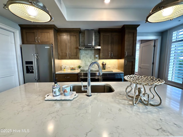 kitchen featuring a sink, tasteful backsplash, wall chimney exhaust hood, high quality fridge, and light stone countertops