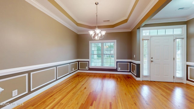 foyer with a decorative wall, a wainscoted wall, wood finished floors, ornamental molding, and a notable chandelier