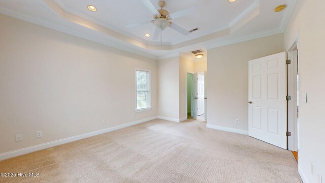 empty room featuring light carpet, crown molding, a raised ceiling, and recessed lighting