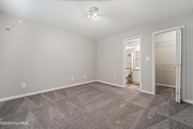 unfurnished bedroom featuring a closet, baseboards, ensuite bath, a walk in closet, and carpet floors