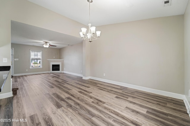unfurnished living room with baseboards, visible vents, ceiling fan with notable chandelier, wood finished floors, and a fireplace
