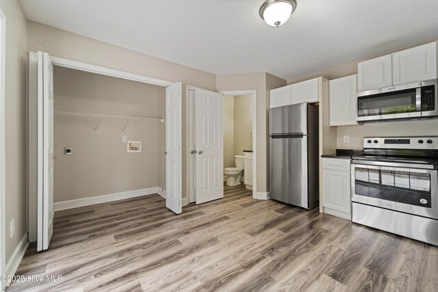 kitchen with light wood finished floors, white cabinetry, baseboards, dark countertops, and appliances with stainless steel finishes