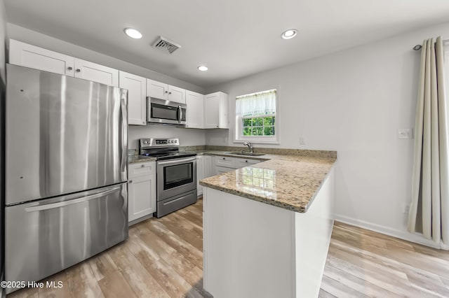 1406 Silverbrook Rd, Oriental, NC 28571 - kitchen with appliances with stainless steel finishes, a peninsula, a sink, white cabinets, and light wood-style flooring