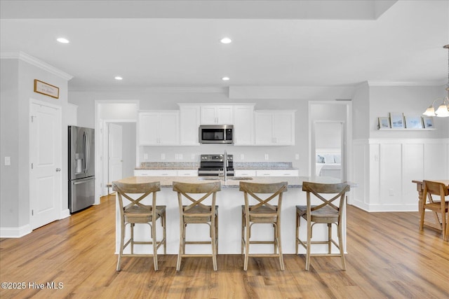 kitchen featuring crown molding, appliances with stainless steel finishes, a kitchen bar, and white cabinetry