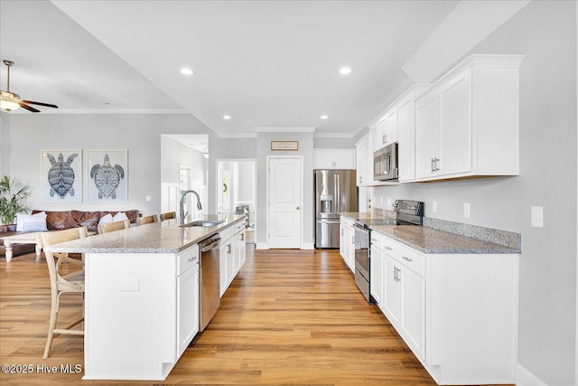kitchen with light wood finished floors, a breakfast bar area, a sink, appliances with stainless steel finishes, and ornamental molding