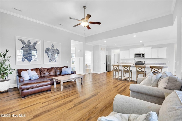 living area with light wood finished floors, ornamental molding, baseboards, and a ceiling fan