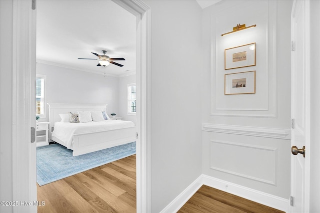bedroom with baseboards, ceiling fan, crown molding, and wood finished floors