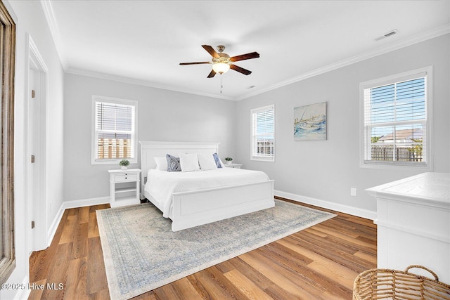 bedroom with visible vents, wood finished floors, baseboards, and ornamental molding