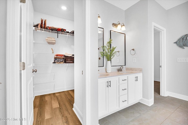 bathroom with a sink, double vanity, a spacious closet, and baseboards