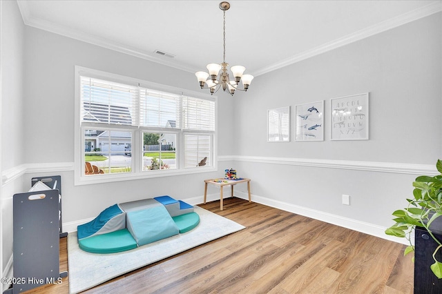 living area with wood finished floors, baseboards, visible vents, crown molding, and a notable chandelier