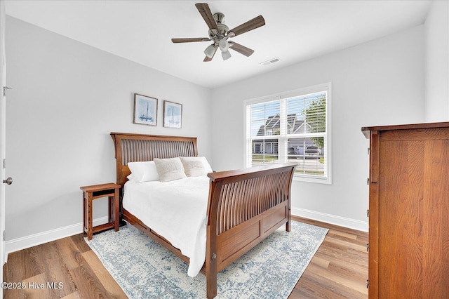 bedroom featuring baseboards, a ceiling fan, visible vents, and wood finished floors