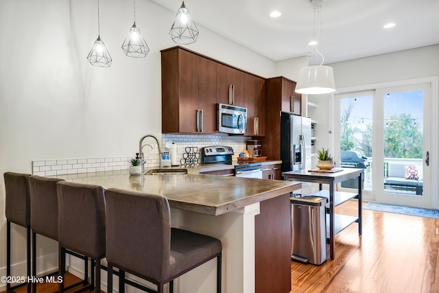 kitchen with stainless steel appliances, a peninsula, backsplash, a breakfast bar area, and light wood-style floors