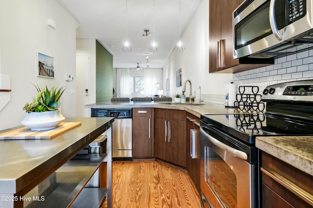 kitchen with appliances with stainless steel finishes, a sink, backsplash, light wood-style floors, and a peninsula