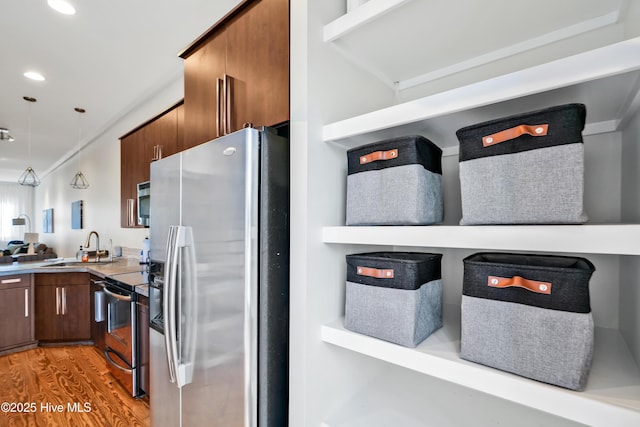 kitchen with stainless steel appliances, a sink, light wood-style floors, pendant lighting, and light countertops