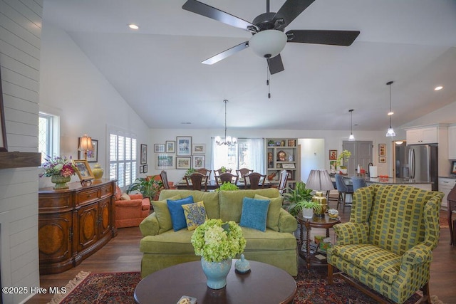 living area featuring high vaulted ceiling, ceiling fan with notable chandelier, and dark wood-style floors
