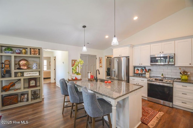kitchen featuring lofted ceiling, stainless steel appliances, light stone counters, decorative backsplash, and white cabinets