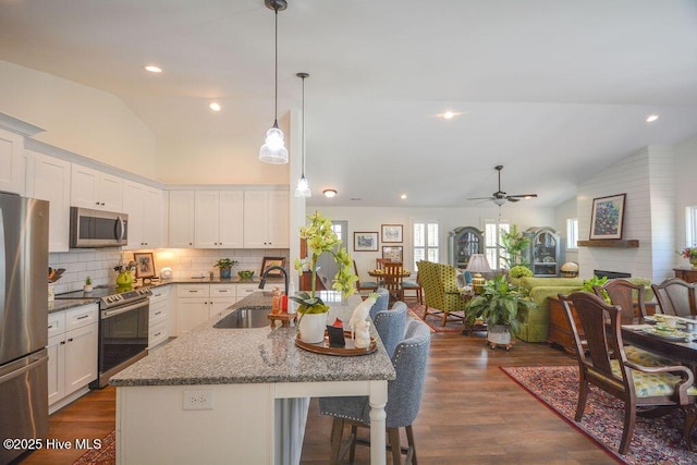 kitchen with vaulted ceiling, stainless steel appliances, white cabinetry, and a sink