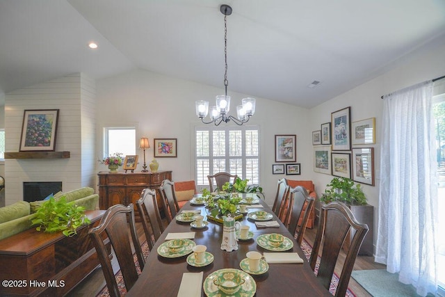 dining room featuring wood finished floors, visible vents, vaulted ceiling, an inviting chandelier, and a fireplace