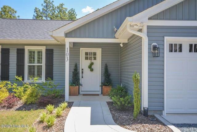 doorway to property with a garage, a shingled roof, and board and batten siding
