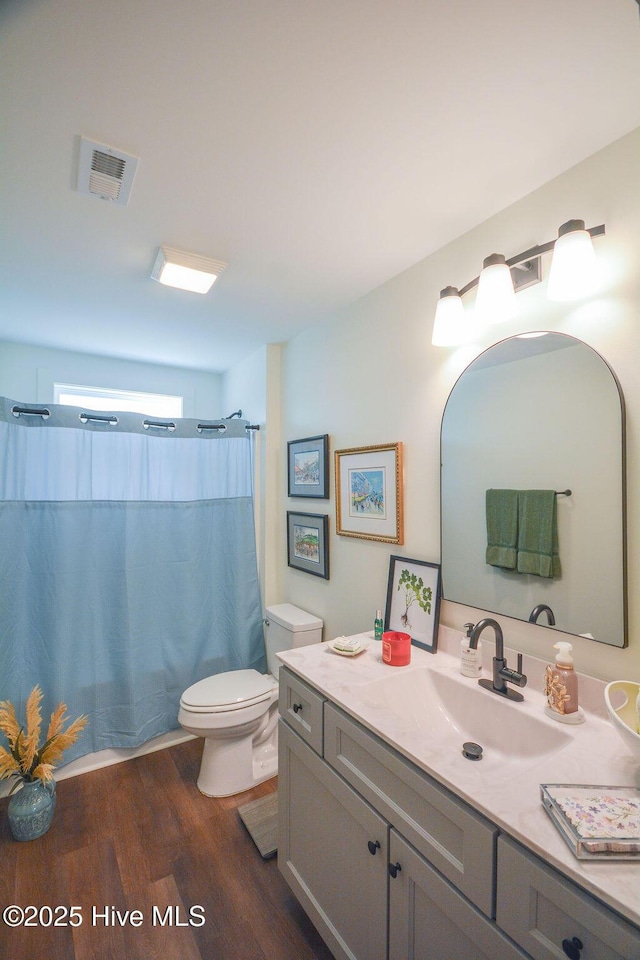 full bath featuring toilet, wood finished floors, curtained shower, visible vents, and vanity