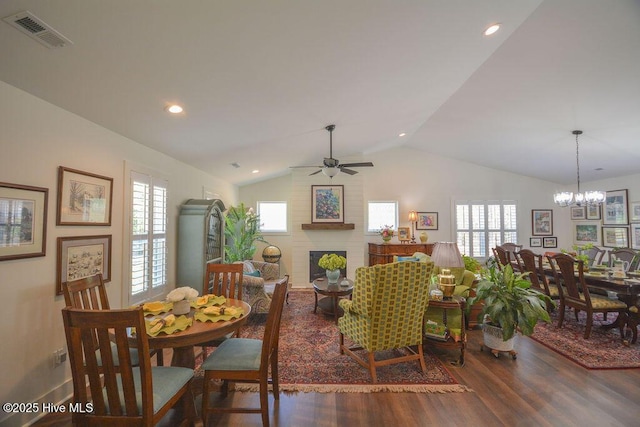 dining room with lofted ceiling, ceiling fan with notable chandelier, wood finished floors, visible vents, and a brick fireplace