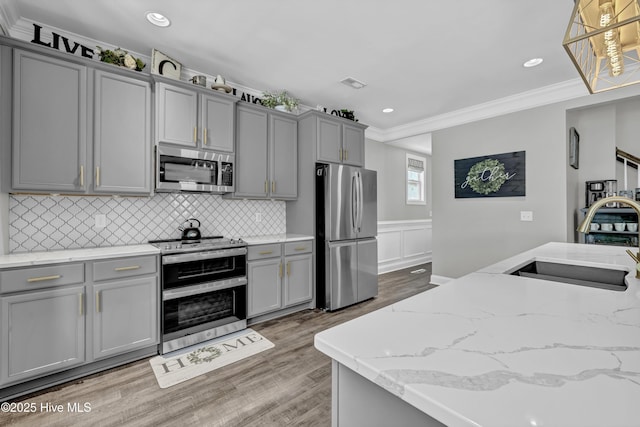 kitchen featuring a sink, light wood-style floors, gray cabinetry, appliances with stainless steel finishes, and ornamental molding