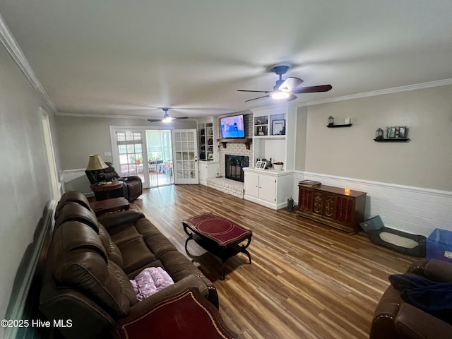 living area with a ceiling fan, wood finished floors, crown molding, a fireplace, and wainscoting