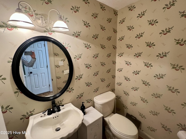 half bath featuring wallpapered walls, a sink, and toilet