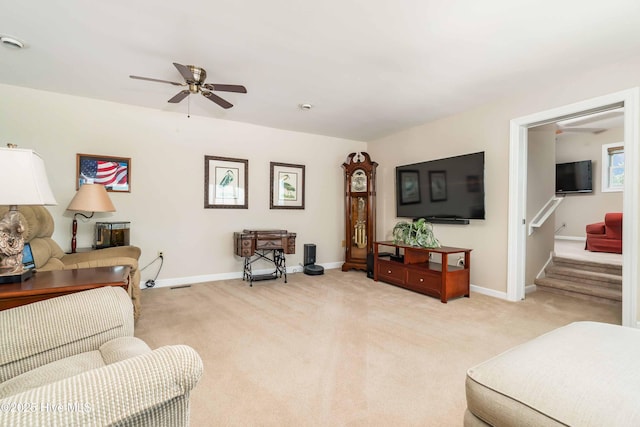 living area with stairway, light carpet, baseboards, and a ceiling fan